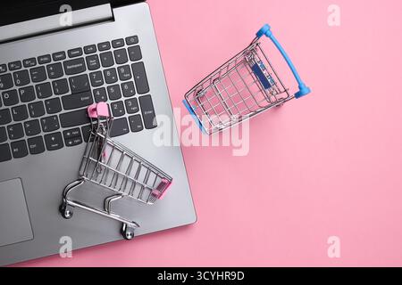 Online-Shopping. Laptop mit Supermarktwagen auf rosa Pastellhintergrund. Draufsicht. Flache Lagen Stockfoto