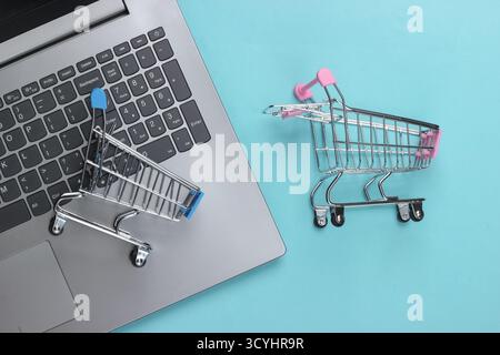 Online-Shopping. Laptop mit Supermarktwagen auf blauem Pastellhintergrund. Draufsicht. Flache Lagen Stockfoto