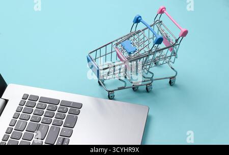 Online-Shopping. Laptop mit Supermarktwagen auf blauem Pastellhintergrund Stockfoto