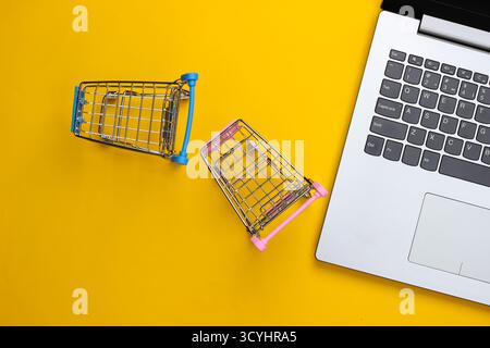 Online-Shopping. Laptop mit Supermarktwagen auf gelbem Hintergrund. Draufsicht. Flache Lagen Stockfoto