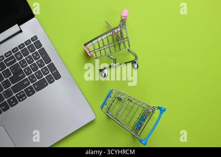 Online-Shopping. Laptop mit Supermarktwagen auf grünem Hintergrund. Draufsicht. Flache Lagen Stockfoto