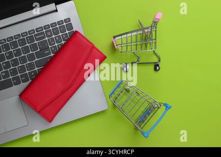 Online-Shopping. Laptop mit Supermarktwagen, Brieftasche auf grünem Hintergrund. Draufsicht. Flache Lagen Stockfoto