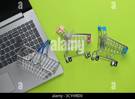 Online-Shopping. Laptop mit Supermarktwagen, Korb auf grünem Hintergrund. Draufsicht. Flache Lagen Stockfoto