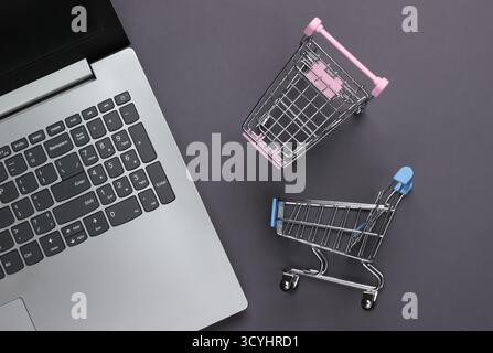 Online-Shopping. Laptop mit Supermarktwagen auf grauem Hintergrund. Draufsicht. Flache Lagen Stockfoto