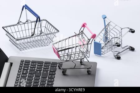 Online-Shopping. Laptop mit Supermarktwagen, Korb auf weißem Hintergrund. Stockfoto