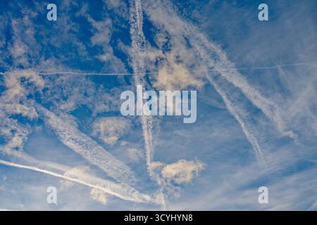 Kondensstreifen, die sich in der Abenddämmerung gegen einen blauen Himmel ausbreiten Stockfoto