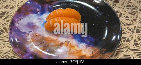 Zwei Stücke frischer Lachs-Nigiri-Sushi, wunderschön präsentiert auf einem Teller mit Galaxienmuster. Stockfoto