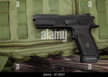 Schwarze halbautomatische Pistole auf olivgrünem taktischem Gurtband und dunkler Holzoberfläche Stockfoto