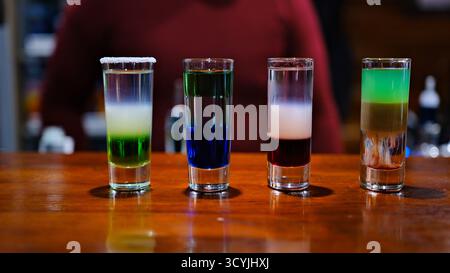 Array Shot Gläser mit lebendigen und farbenfrohen Getränken stehen auf einer eleganten Bartheke. Verschiedene Farbtöne reflektieren das Licht und schaffen eine energiegeladene Atmosphäre, perfekt für einen Abend. Stockfoto