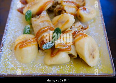 Crepes gefüllt mit Schokoladenaufstrich und Banane auf weißem Teller. Dünne Pfannkuchen, Blini. Süßes Dessert. Hochwertige Fotos Stockfoto
