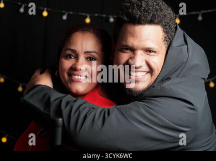 Ein Mann und eine Frau umarmen sich. Der Mann trägt einen schwarzen Hoodie. Die Frau trägt einen roten Pullover Stockfoto