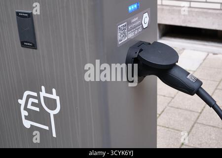 Nahaufnahme einer Ladestation für Elektrofahrzeuge mit eingestecktem Kabel und Straßenbelag im Hintergrund Stockfoto