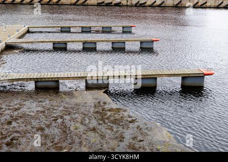 Über dem Kopf von drei parallelen leeren Holzpontons oder Docks, die sich über dunklem Wasser erstrecken, mit einem Abschnitt von trübem Algenwasser darunter. Stockfoto