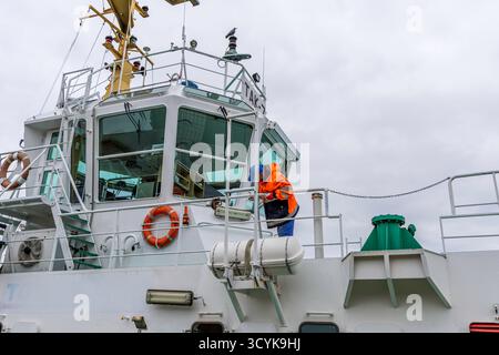 Eine Nahaufnahme des roten Rumpfes, des weißen Daches und des Geländes eines großen Fracht- oder Dienstschiffes, das sicher an einem Pier in einem Industriehafen auf einem Clo angedockt ist Stockfoto
