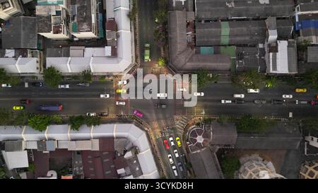 Ein direktes Luftbild über dem Kopf (von oben nach unten), das eine geschäftige Straßenkreuzung in Bangkok erfasst. Fahrzeuge erzeugen kleine Lichtstreifen, die veranschaulichen Stockfoto