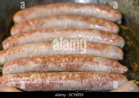 Bei einer horizontalen Nahaufnahme wird eine Reihe roher Würstchen in einer Pfanne mit geringer Schärfentiefe gezeigt. Stockfoto