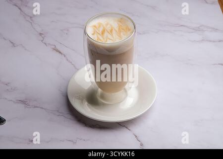 Genießen Sie den köstlichen Caramel Latte, der wunderschön in einem klaren Glas auf einer Marmoroberfläche präsentiert wird Stockfoto