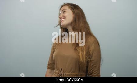 Die Frau zeigt ein weiches Profil, während sie sich seitwärts dreht, während sie im Studio mit hellblauem Hintergrund lächelt; Glück. Stockfoto