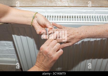Eine Pflegekraft schneidet sorgfältig die Nägel einer älteren Frau mit einer Nagelschere ab, um sie persönlich zu versorgen und zu unterstützen. Stockfoto
