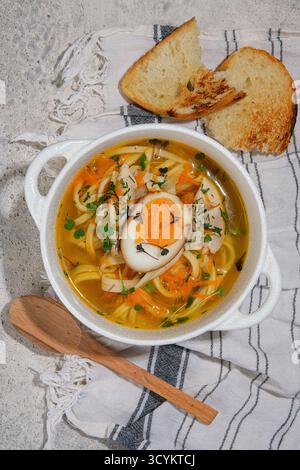 Genießen Sie eine gemütliche Schüssel köstlicher Hühnchennudelsuppe mit Ei und frisch geröstetem Brot Stockfoto