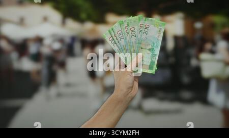 Hand hält russische Rubel im Freien mit einem verschwommenen Hintergrund der Stadtstraße, erfasst städtische Finanzkonzepte und männliche Darstellung im öffentlichen Verkehr Stockfoto