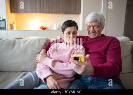 Konzentrierte Seniorenfamilie, die Webfeeds ansieht, Videoanrufe auf dem Smartphone auf dem Sofa, aktives Seniorenleben Stockfoto