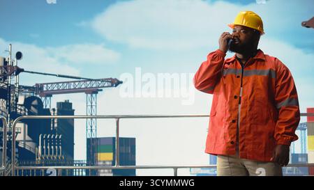 Porträt eines lächelnden Offshore-Bohringenieurs, der Umweltverträglichkeitsprüfungen durchführt und im Walkie-Talkie spricht. Happy Expert verfolgt den CO2-Fußabdruck und kommuniziert über Funkübertragung, Stockfoto