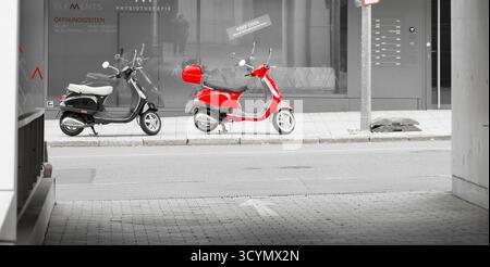 Stuttgart, Deutschland, 10.18.2025; Farbtastenfoto mit einem roten Moped auf einer Stadtstraße, durch ein Tor gesehen, mit der Umgebung in schwarz-weiß Stockfoto