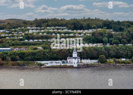 GREENOCK, SCHOTTLAND - 19. August 2024: Der Leuchtturm von Cloch Point bewacht den Firth of Clyde, während sich Reihenhäuser auf dem Hügel über dem friedlichen Gelände befinden Stockfoto