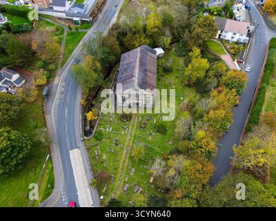 Blick aus einem hohen Winkel auf eine walisische Kirche, umgeben von Herbstbäumen und einem Friedhof Stockfoto