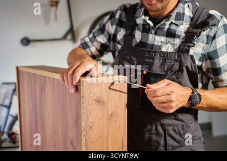 Nahaufnahme des Zimmermanns mit Inbusschlüssel beim Zusammenbau von Holzmöbeln in der Werkstatt. Man verwendet den Innensechskantschlüssel zum Festziehen der Schrauben. Das Konzept der Zimmerei und des Pelzes Stockfoto