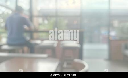 Extrem weich fokussiertes horizontales Bild für die Aufnahme moderner Cafés im Innenraum, ideal für die Verwendung von dezentem Hintergrund. Verschwommene Figur ist links im Hintergrund sichtbar Stockfoto