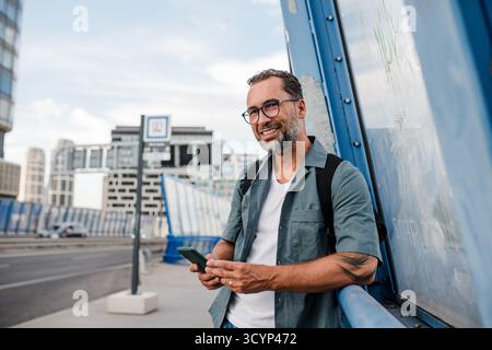 Bärtiger Mann, der das Telefon benutzt, während er auf den Bus wartet. Stockfoto