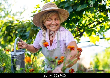 Lächelnde Seniorin, die Blumen im Garten tränkt. Stockfoto
