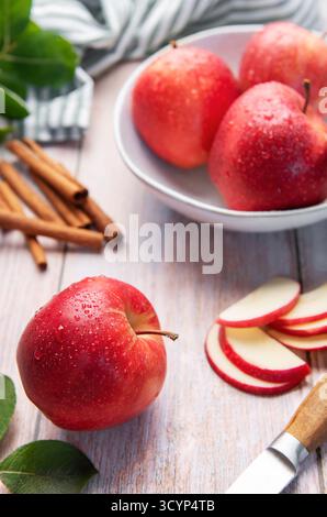 Rote Äpfel, Zimtstangen und geschnittene Äpfel auf einer Holzoberfläche, bereit zum Kochen Stockfoto