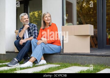 Ein älteres Ehepaar, das sich nach dem Umzug auf der Veranda neben verpackten Kisten ausruhen konnte Stockfoto