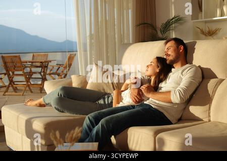 Entspanntes verliebtes Paar, das zu Hause auf einer Couch sitzt und über Sonnenuntergang nachdenkt Stockfoto