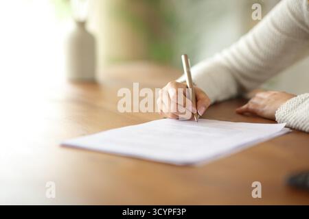 Nahaufnahme Porträt einer Frau, die zu Hause ein Papierformular oder einen Vertrag auf einem Holztisch unterschreibt Stockfoto