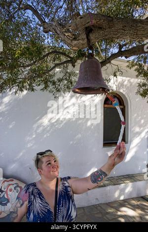 Frau, die eine Glocke läutet, sagt, dass sie Glück für eine Zukunft der Ehe geben soll.Agios Loannis Kapelle auf Skopelos, eine beliebte Touristenattraktion, die durch den Mamma Mia Film berühmt wurde. Stockfoto