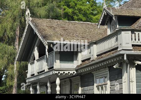 Ein charmantes Holzgebäude mit detaillierten Balkonen und traditioneller Architektur, eingebettet zwischen hohen Bäumen unter klarem blauem Himmel, stellt einen dar Stockfoto