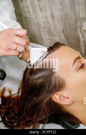 Eine Nahaufnahme der Hand eines Friseurs, der ein Peeling, eine Maske oder eine Farbe auf das Haar in einem Friseur aufträgt Stockfoto