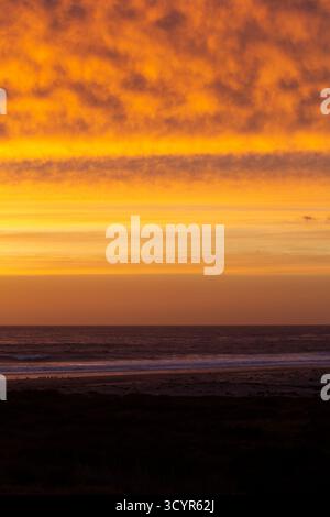 Bewölkter goldener Sonnenuntergang über dem Pazifik und dem Sandstrand. Stockfoto