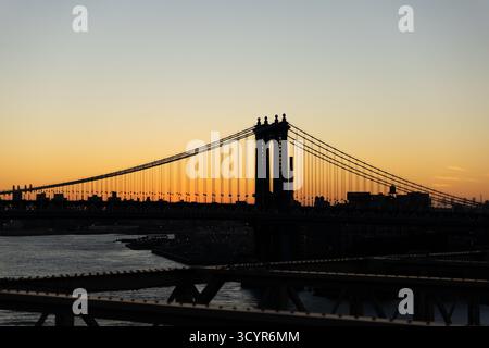 Die legendäre Manhattan Bridge steht vor einem warmen, abfallenden Sonnenaufgangshimmel über dem East River in New York City. Stockfoto