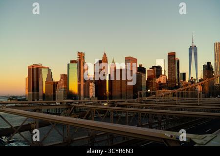 Die Skyline von Lower Manhattan, einschließlich der markanten Wolkenkratzer, strahlt mit goldenem Licht, das bei Sonnenaufgang von Gebäuden reflektiert wird, vom Brooklyn B aus gesehen Stockfoto