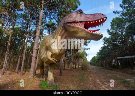 Große, lebensechte Tyrannosaurus rex-Skulptur im Waldpark mit Besuchern, die auf einem Pfad spazieren und die Ausstellung im Dino Parque, Lourinhã, beobachten Stockfoto