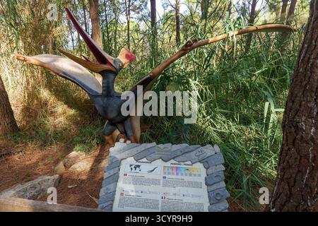 Eine große Pteranodon-Pterosaurier-Statue mit ausgebreiteten Flügeln in einem üppigen Wald, begleitet von einer informativen Tafel. Stockfoto