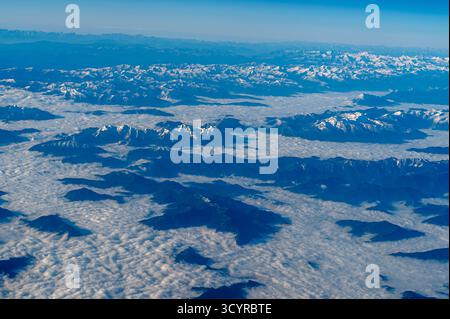 Bewundern Sie eine atemberaubende Luftlandschaft mit majestätischen, schneebedeckten Bergen, die über einem riesigen Wolkenmeer ragen Stockfoto