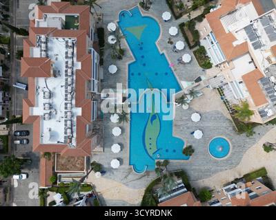 Blick aus der Vogelperspektive auf einen großen Swimmingpool mit einzigartigem Design in einem von Gebäuden und Palmen umgebenen Resort Stockfoto