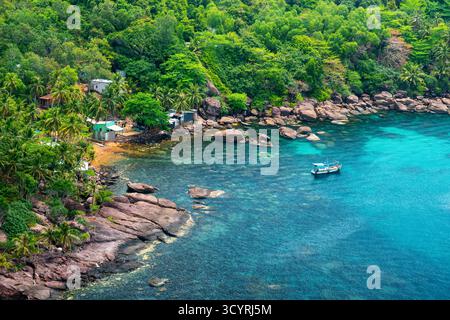 Versteckte tropische Bucht auf Phu Quoc Island, Vietnam, umgeben von üppig grünem Regenwald, Palmen und klarem türkisfarbenem Wasser Meer mit einem kleinen Fischerboot Stockfoto