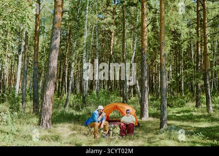 Paare, die sich in der Nähe des Zeltes entspannen, während sie im Wald im Freien campen Stockfoto